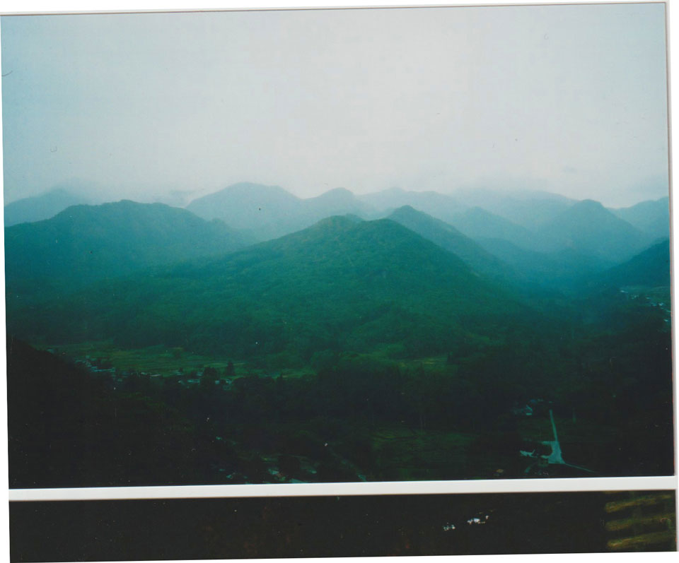 Mist-covered green mountains fading into the distance under a pale sky.